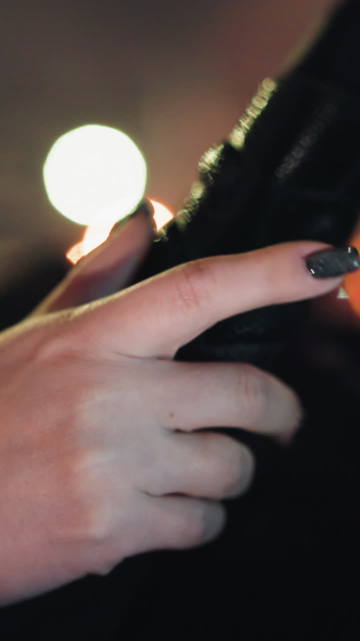 First-person view of a woman's hand with black painted nails tapping on a steering wheel at night. The background features colorful, blurry city lights