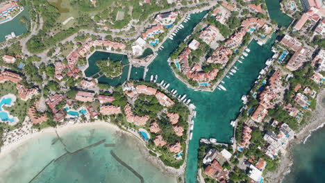 Stunning-Bird's-Eye-View-of-a-Marina-Featuring-Yachts,-Holiday-Condominiums,-and-a-Serene-Sea-with-Shadows-of-Passing-Clouds