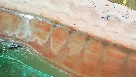 aerial bird’s-eye drone view looking straight down on busy saco, maine beaches. crowds fill sandy shores near vacation homes as atlantic ocean waves crash along the lively coastline