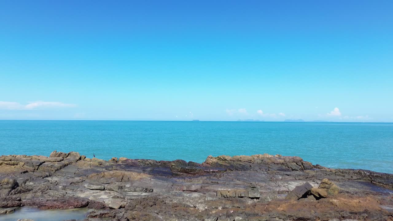 Luftaufnahmen einer Drohne von einem einsamen Vogel, der sich an einer felsigen Küstenlinie auf Koh Lanta ausruht, mit dem offenen Meer im Hintergrund, wodurch eine minimalistische und friedliche Küstenwildtierszene ohne Menschen entsteht