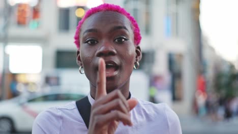 young woman with pink hair making a shhh gesture and smiling