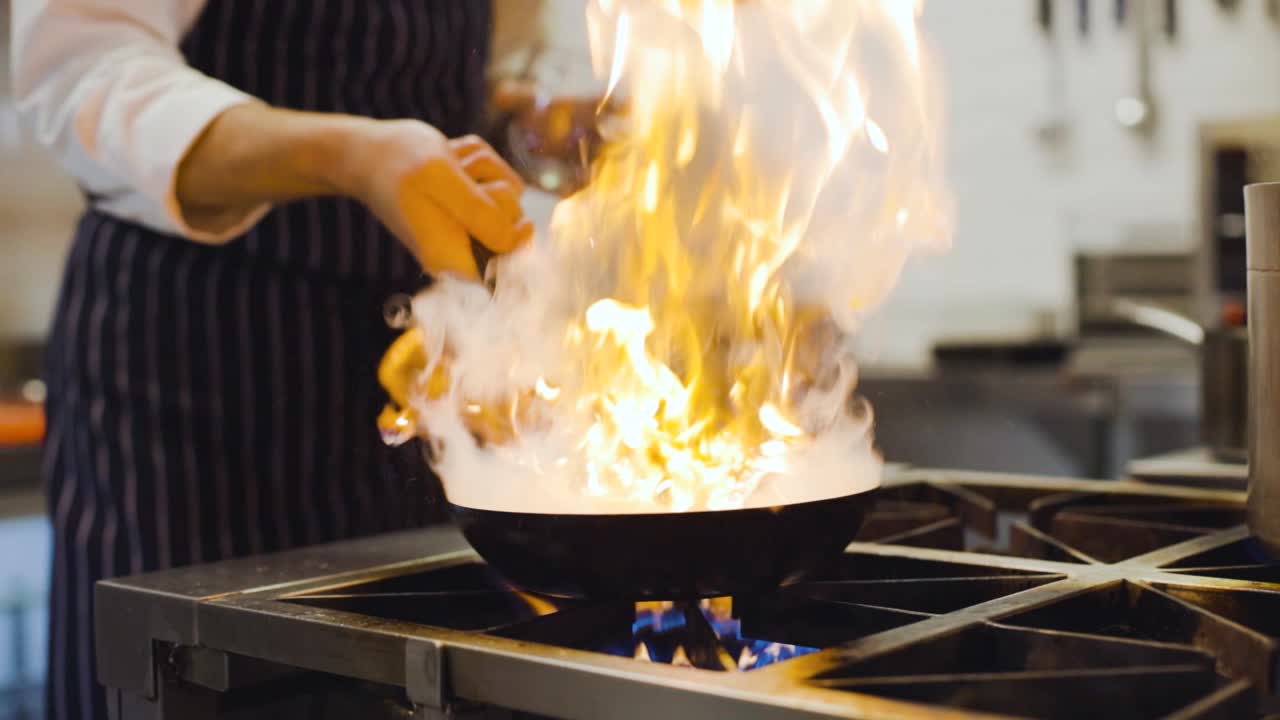 Slow motion: chef che infiamma una padella in una cucina professionale, primo piano sulla padella.