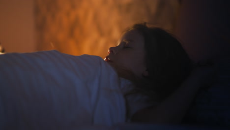 Little-girl-sleeps-on-bed-in-room-with-glowing-night-lamp