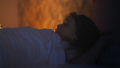 little girl sleeps on bed in room with glowing night lamp