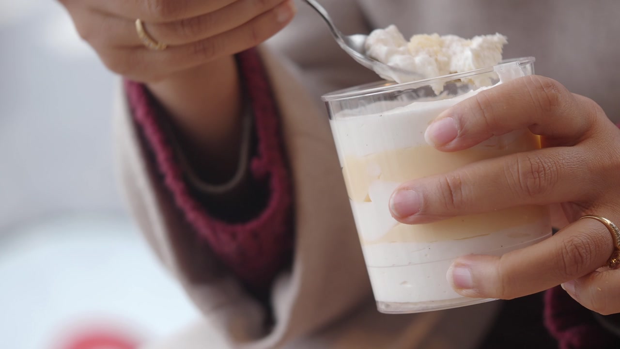 Close-up of Hand Eating Layered Cream Dessert with a Spoon