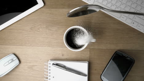 teaspoon of sugar powder being spilled into and around a cup of coffee