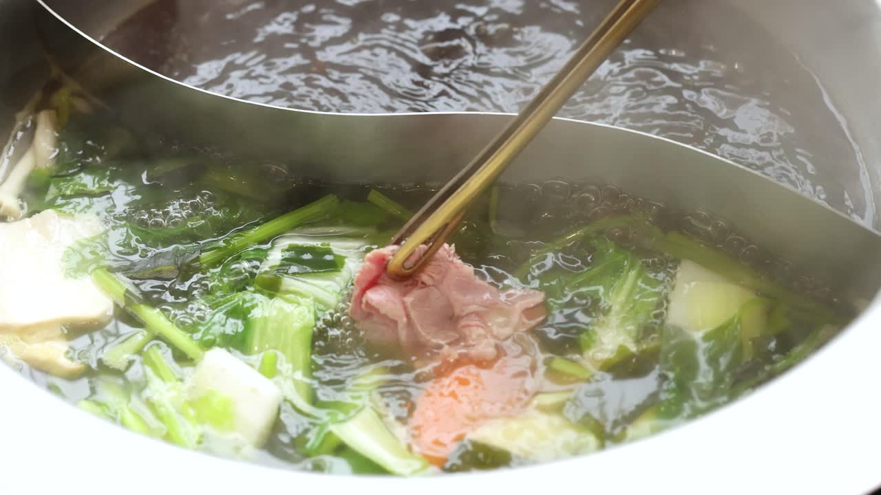 Chopsticks swirl beef slice in steaming dual broth hotpot with vegetables, bright natural lighting
