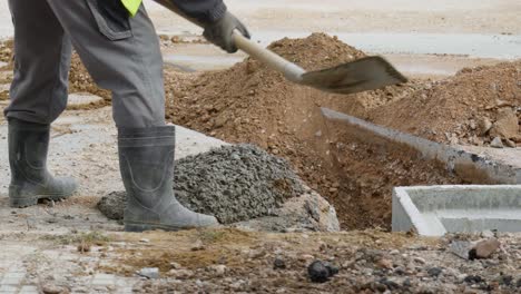 male construction worker pouring cement concrete with shovel around precast concrete pit for new drainage pipe system for roads