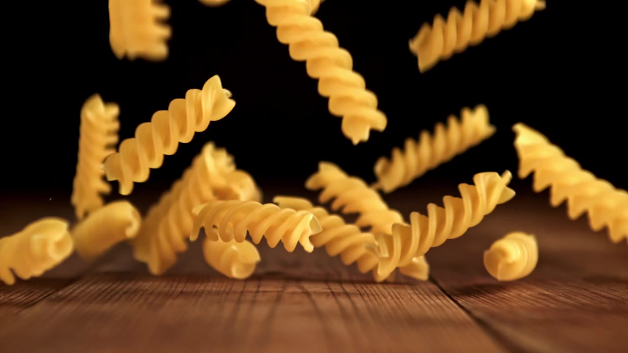 Raw Fusilli Pasta Falling in Slow Motion onto a Wooden Table