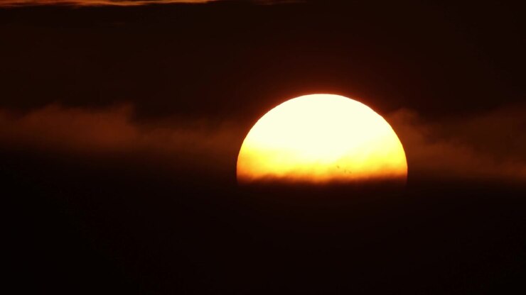 A huge yellow round sun sets behind black clouds