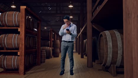 full body of asian male professional worker with his smartphone in cellar of winery, he is nodding his head with dissapionted