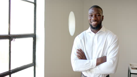 smiling african american businessman in white shirt standing with arms crossed in office