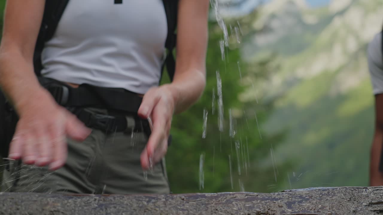 Hiker rinses hands with water from a spring in the Robanov Kot valley on a summer day in Slovenia