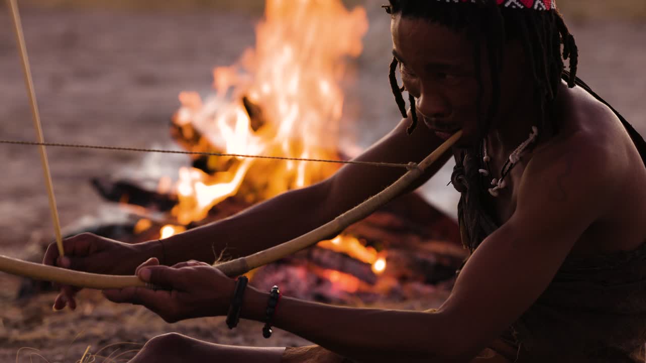 retrato en primer plano de la gente de san (bushmen) tocando un instrumento musical tradicional al atardecer alrededor de un fuego