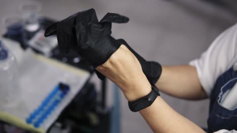High-angle-footage-of-female-tattoo-master-puts-on-black-rubber-gloves-and-prepares-to-do-a-tattoo-for-her-client.-Wearing-black-sport-watches.-Slow-motion