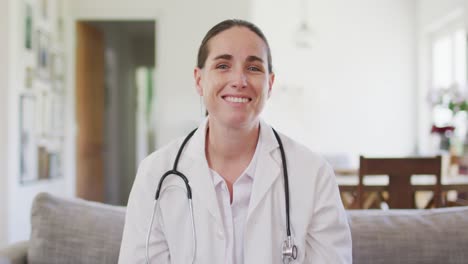 Happy-caucasian-female-doctor-sitting-on-sofa-having-video-call