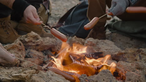 hands of a group of teenage friends roasting sausages on the bonfire