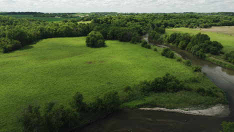 Lush-Green-Meadow-And-Forest-With-River-In-Daytime