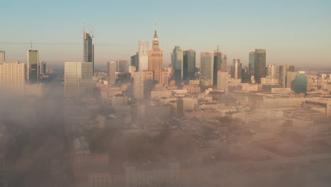 Amazing-shot-of-downtown-panorama-coming-out-from-dense-fog.-Group-of-high-rise-buildings-lit-by-morning-sun.-Warsaw,-Poland
