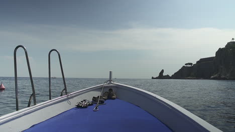 Front-of-tour-boat-cruising-along-Mediterranean-cliff-coast,-shoes-on-deck,-slow-motion