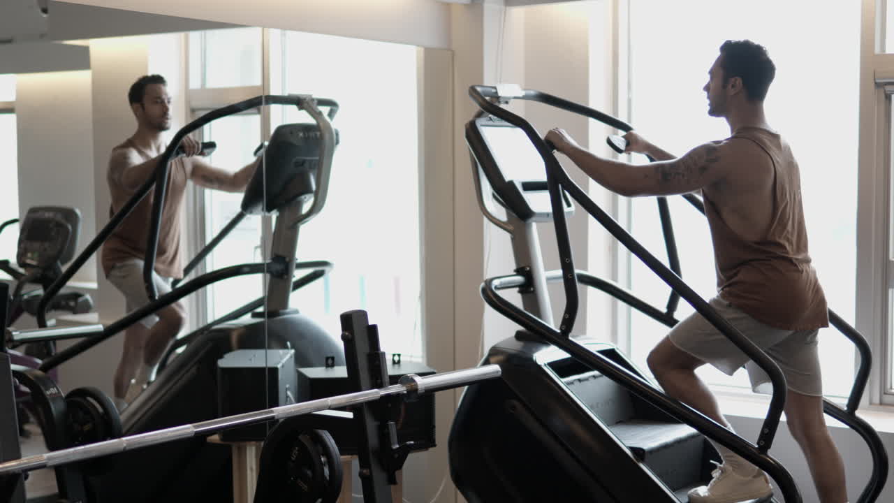 Uomo sportivo che fa cardio su una macchina stepper in palestra, un uomo riflesso nello specchio che usa l'attrezzatura Stepmill per la salita delle scale - rallentatore