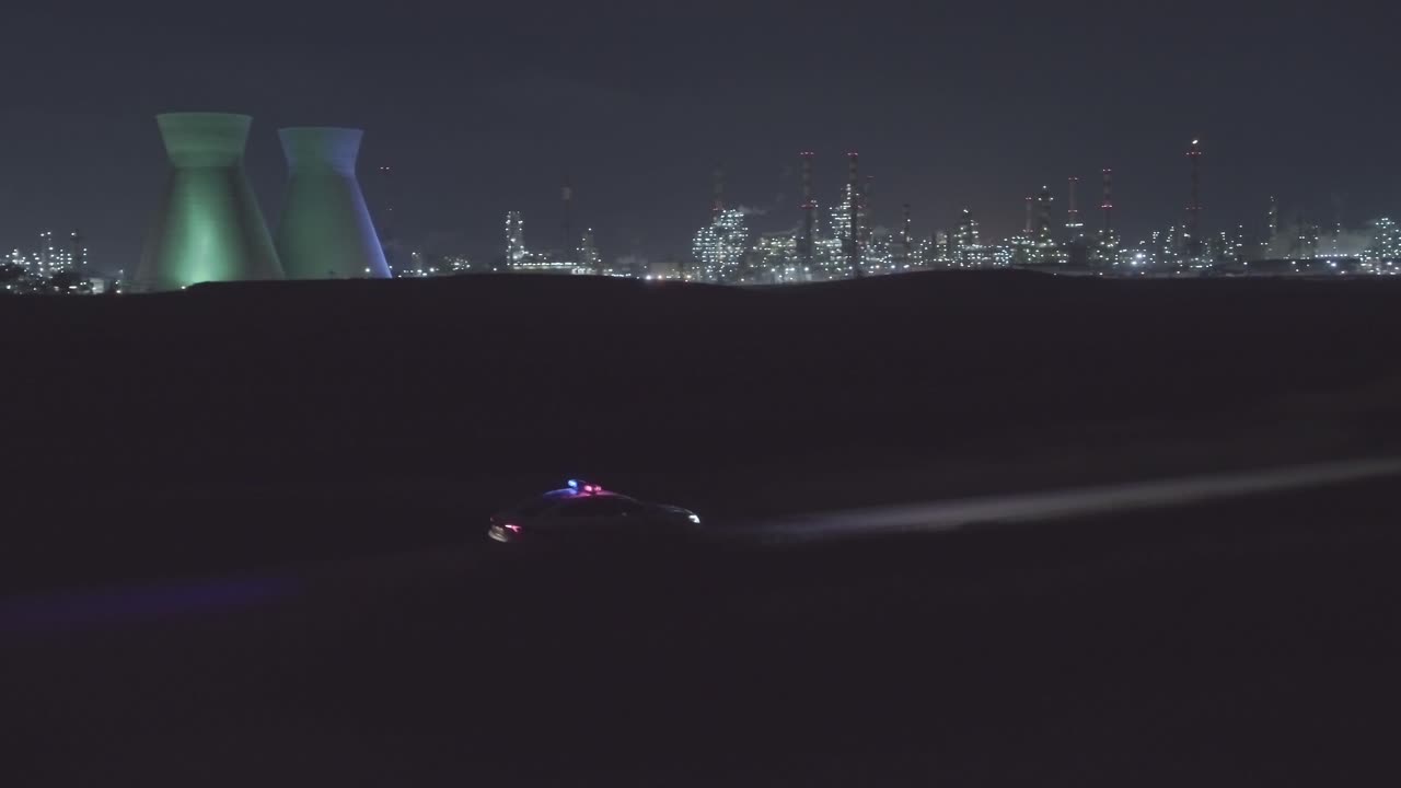 Night aerial footage of a police car driving down a dark urban area