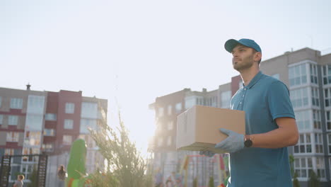 Blue-delivery-man-send-a-package-to-customer-on-before-deliver-cargo.-4k-resolution-and-slow-motion-shot.-Male-postman-with-parcel-in-hands-at-city-street.-Postal-concept.-Delivery-service.