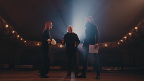 actors acting out quarrel in spotlight zoom in view of elderly man taunting arguing couple in spotlight during play rehearsal on stage in theater