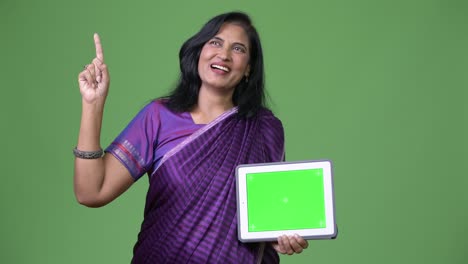 mature happy beautiful indian woman thinking while showing digital tablet and pointing finger up