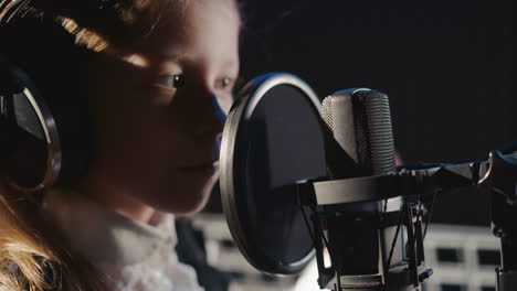 kid touches microphone in recording studio. inquisitive young girl in headphones inspects microphone by finger in acoustically isolated room