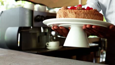 Mid-section-of-waiter-holding-strawberry-pie-on-cake-stand