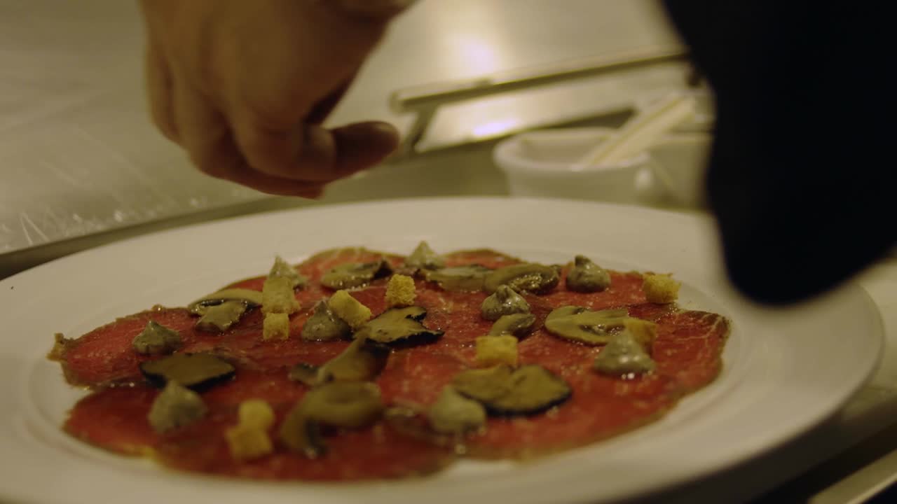 Close up of chef's hand putting topping on delicious food on plate at restaurant