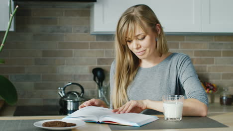 young attractive woman reading a book in the kitchen nearby stands a glass of milk concept - healthy