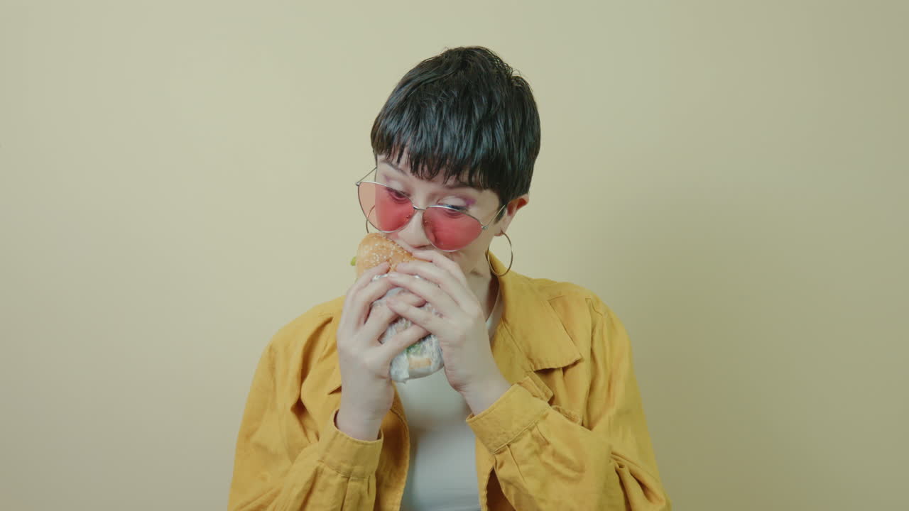 Modern short-haired woman voraciously chomping a burger in a studio background