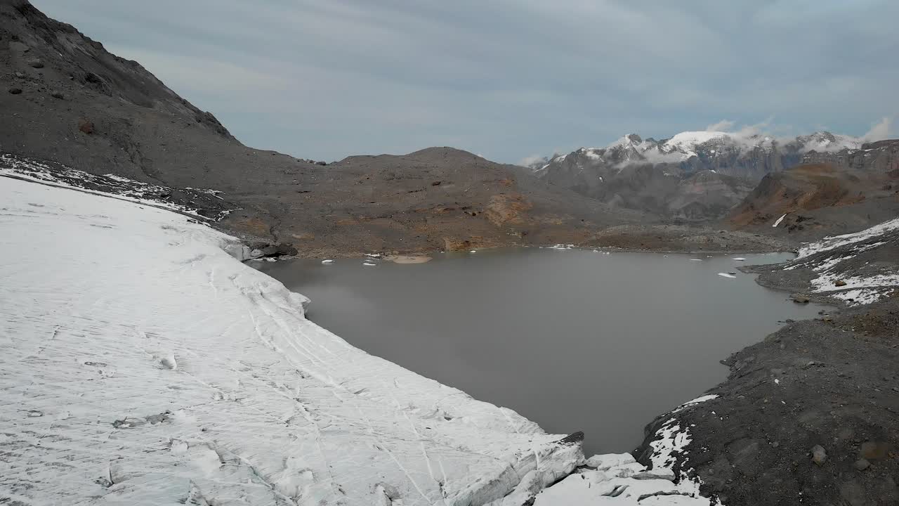 vuelo aéreo sobre el hielo del glaciar y el lago glacial en el glaciar claridenfirn en uri, suiza con una vista de icebergs flotantes en el agua, grietas en el hielo y picos en la distancia