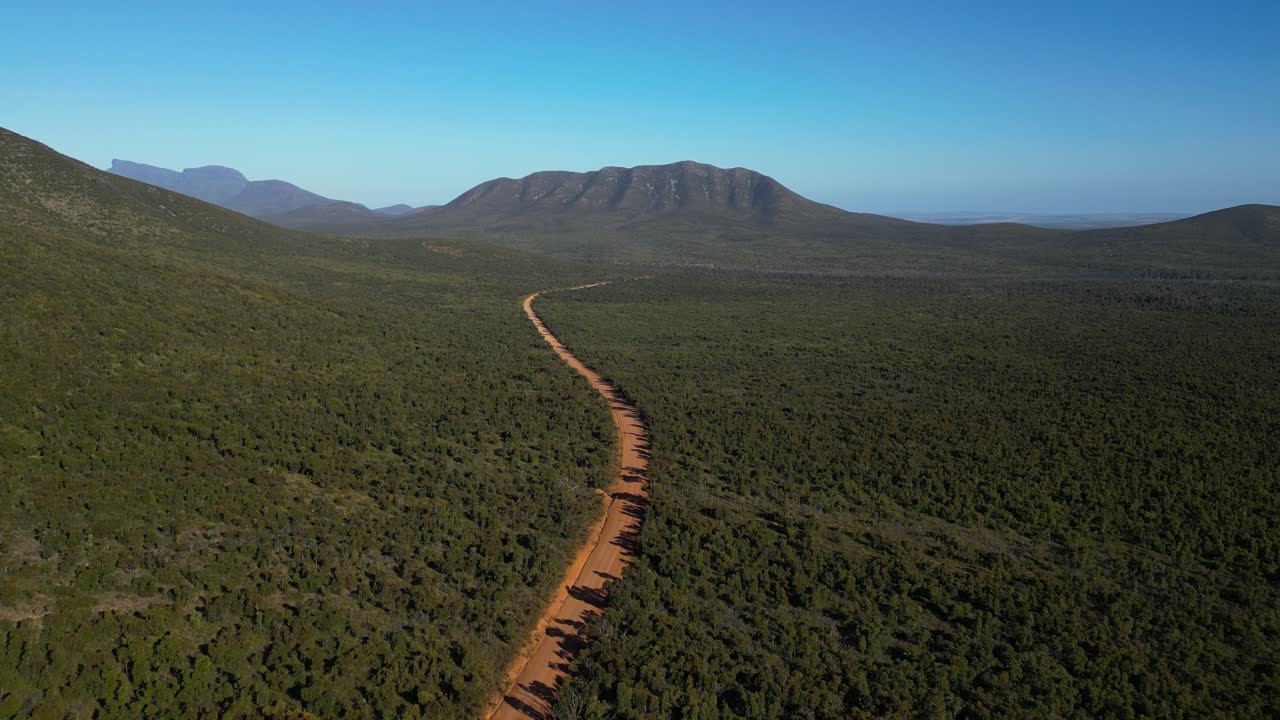 toma aérea siguiendo un camino de tierra rojo vacío con montaña a distancia en el interior de australia