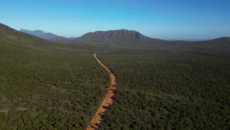 Aerial-shot-following-empty-red-dirt-road-with-moutain-in-distance-in-Australian-outback