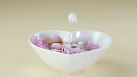 mini chocolate eggs dropped into a heart shaped bowl in slow motion