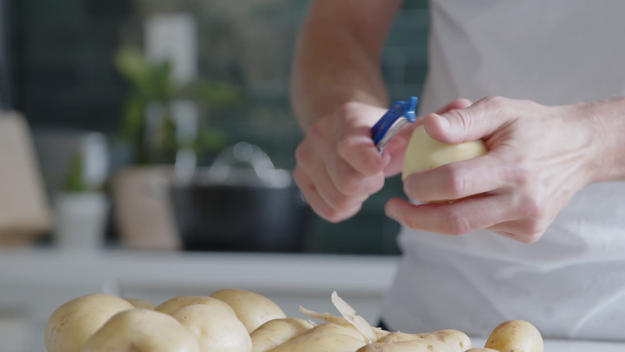 primer plano de un hombre pelando papas frescas con un pelador en una cocina moderna