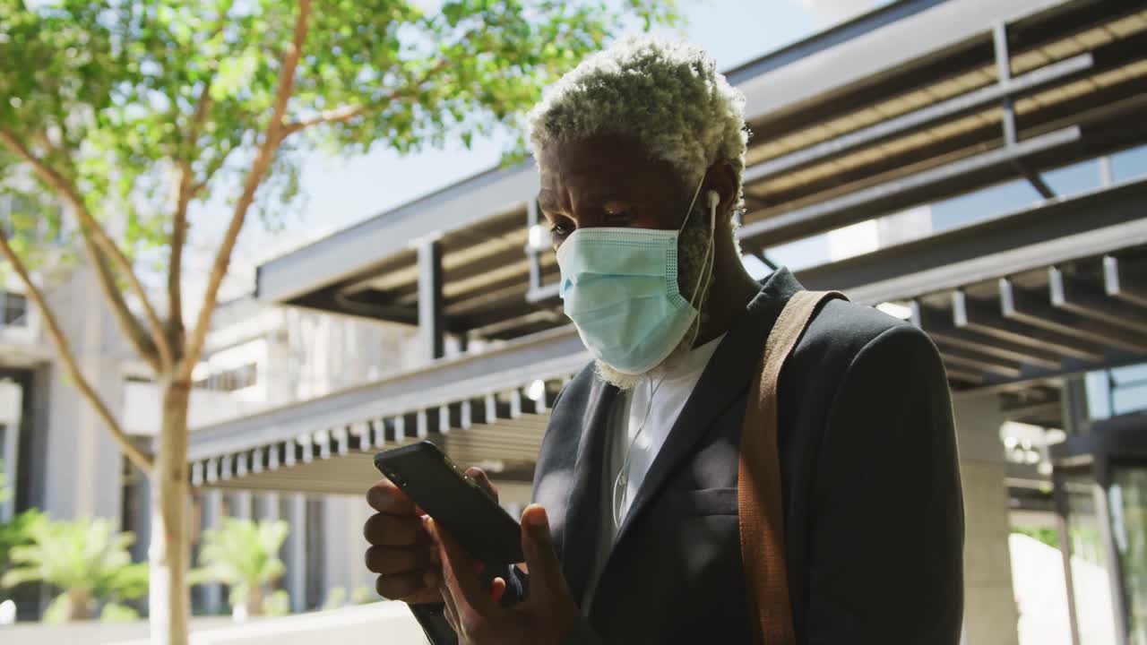 African american senior man wearing face mask using smartphone in corporate park