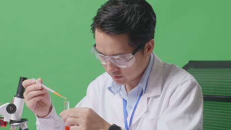 close up of side view of asian man scientist making experiment with test tube and saying wow while working on the table with microscope in the green screen background laboratory