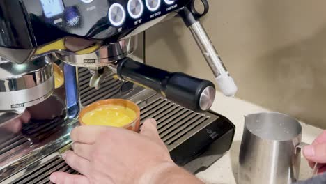 hands prepare coffee using a machine, steaming milk, and pouring into a cup. bright kitchen lighting enhances the process