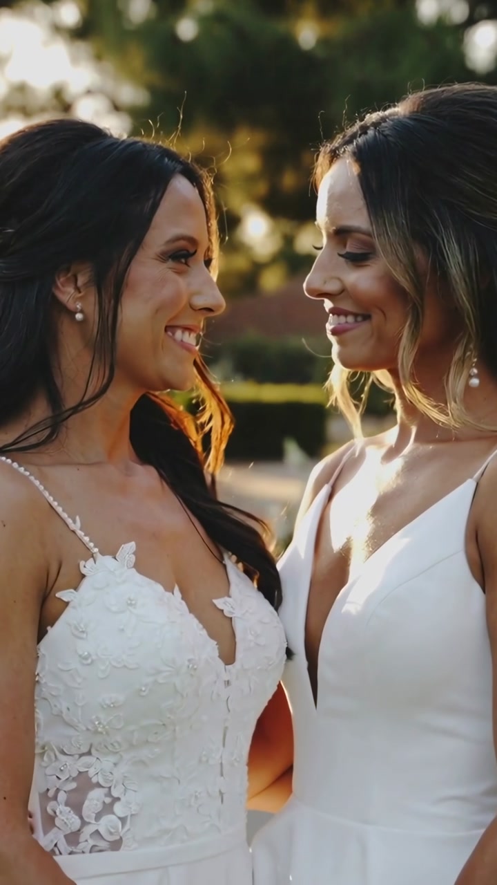 Vertical video: Holding hands two women smiling in garden, wearing gowns, posing, camera tightening