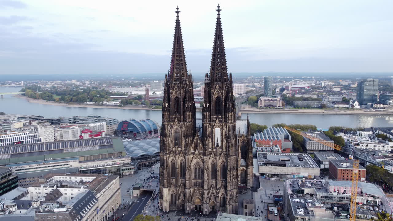 Grand Cologne Cathedral overlooks city skyline and Rhine river bank, aerial arc