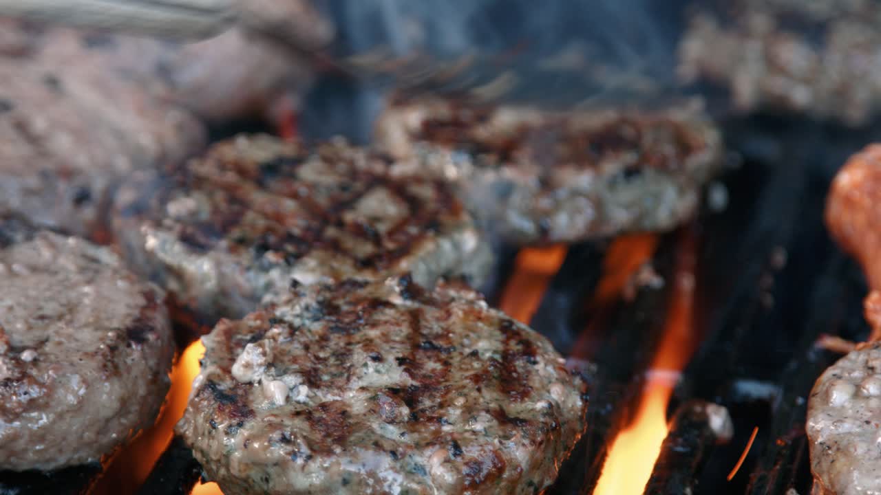 hamburguesas de carne siendo grilladas a la llama y volteadas en barbacoa