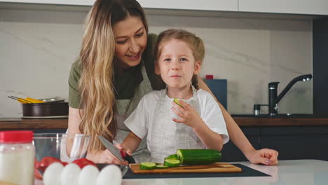 little girl eats cucumber slice cooking salad with mother