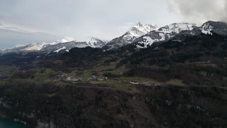 Pintorescas-Casas-Blancas-En-La-Meseta-Miran-Hacia-Walensee,-Suiza,-En-La-Base-De-Las-Montañas-Cubiertas-De-Nieve