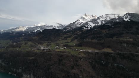 casas blancas pintorescas en la meseta miran hacia abajo en el lago walensee suiza en la base de las crestas montañosas cubiertas de nieve