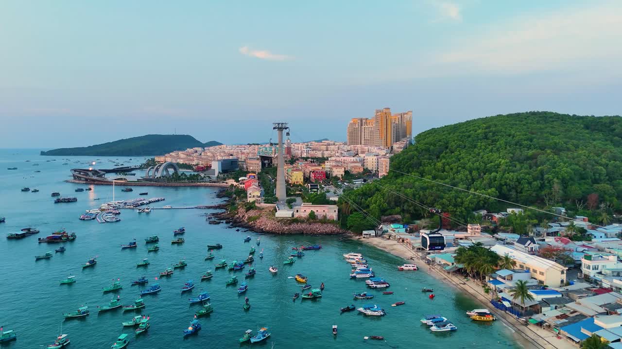 Aerial: fisher village with cable cars, fish boats and Sunset Town cityscape during the day in Phu Quoc Island, Vietnam, establishing drone shot