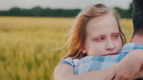 the child clings to his father's shoulder in the background a strong wind swaying wheat